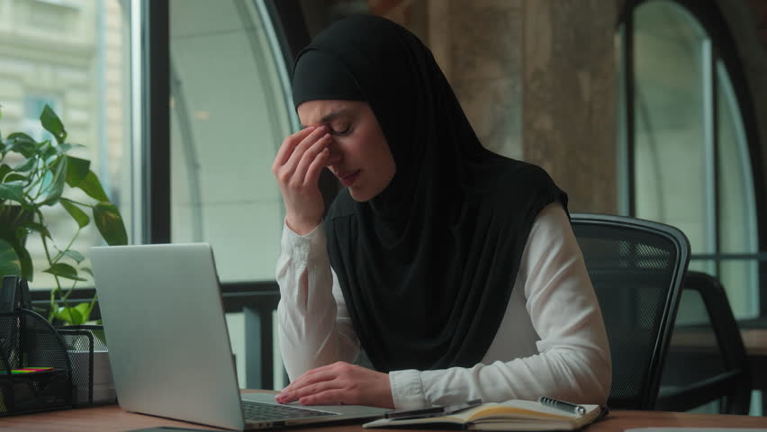 Bad feeling Muslim islamic business woman female girl businesswoman in hijab suffering migraine headache eyes discomfort pain overworked with laptop computer irritated eye in office problem eyesight