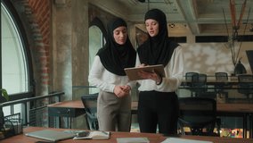 Two business women in office in hijabs Arabian businesswomen muslim islamic female girls managers partners talking architect discussing plan job project with computer digital tablet pointing in front - Powered by Shutterstock - Get 15% off with code: PIKWIZARD15