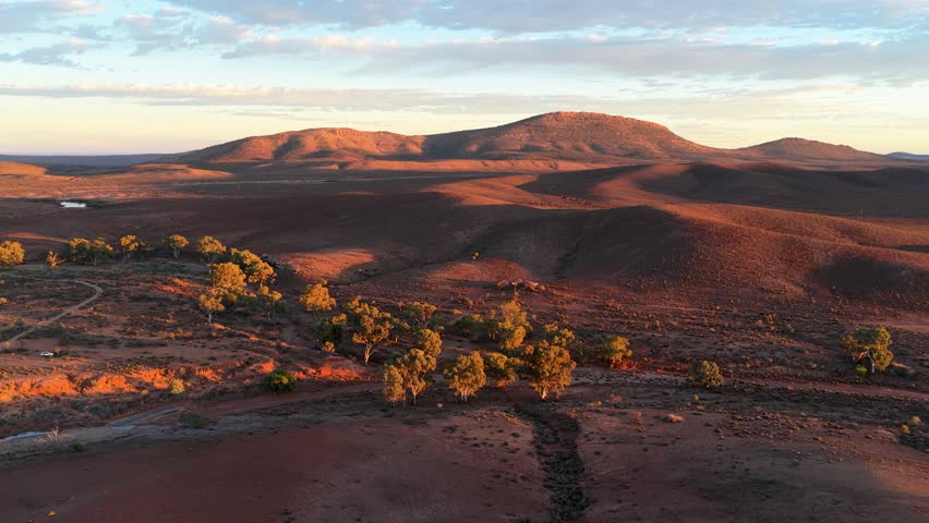 Drone shot of arid outback landscape with winding dry creek bed and sunlit hills, Flinders Ranges, South Australia
