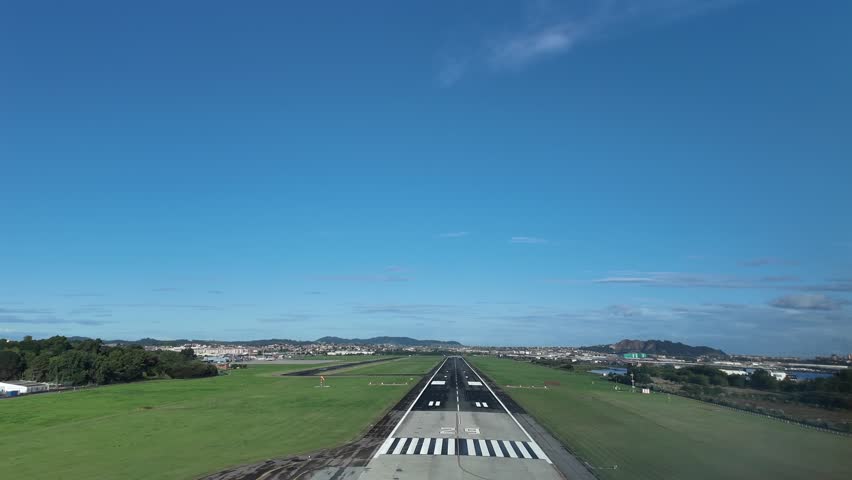 An immersive pilot’s eye view FPV in a real time landing at Santander airport runway, surroended by green fileds , under a bright, unclouded blue sky.
