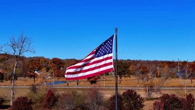 Slow Motion Aerial View, United States flag waving in the wind with colorful autumn trees, vehicles and a bright blue sky in the background, symbolizing patriotism and freedom - Powered by Shutterstock - Get 15% off with code: PIKWIZARD15