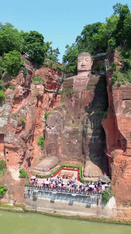Leshan, China: Aerial drone footage of tourists visit the impressive Leshan giant Buddha stone statue in Sichuan in China on a sunny day. Shot with an upward and tilt down motion