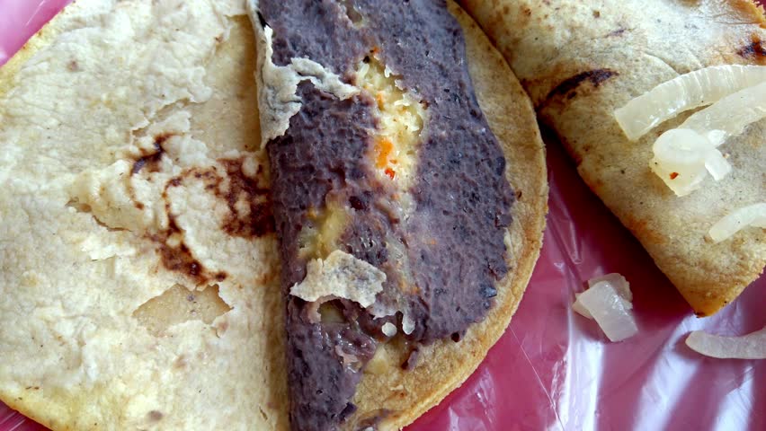 Close up of a taco prepared with beans and yellow sauce served on a red plate.