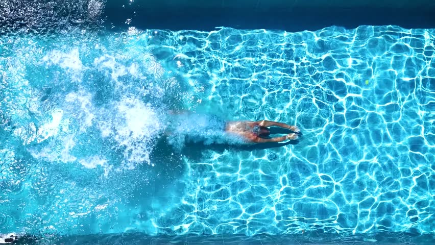 Aerial overhead slow motion view of a man jumping and diving into a swimming pool during summer time