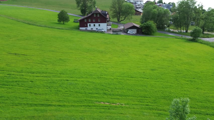 A  stunning green field with a bright red rustic house  at Le Lieu , Switzerland , illustrating rural charm and the beauty of simplicity in the countryside, us01