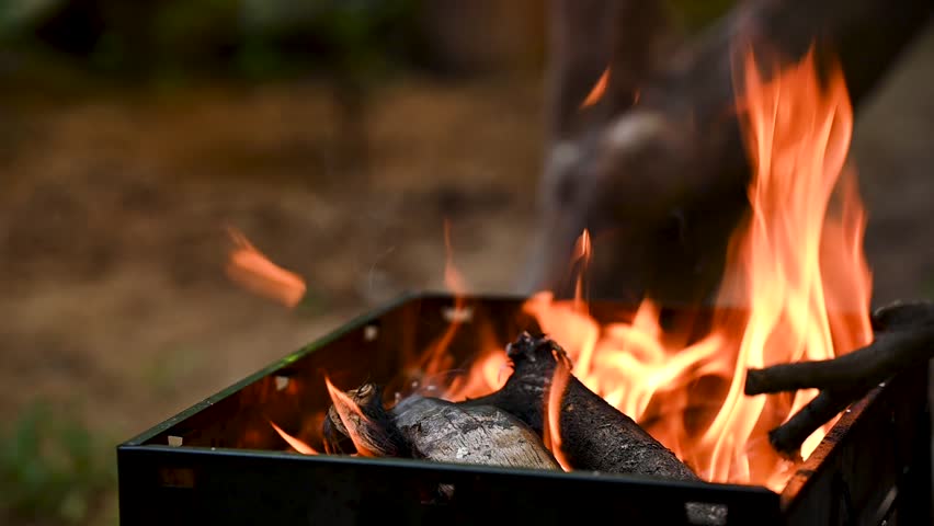 Slow-motion footage of wood burning in a barbecue grill, flames rising to create perfect heat for outdoor cooking. Great for food, barbecue, camping, lifestyle, and sustainable cooking themes.