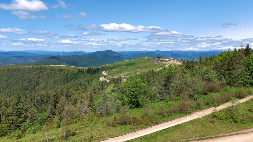 Mountain landscape with forest and dirt roads. Panoramic view of a green mountainous landscape featuring dense forests, winding dirt roads, and distant hills under a bright blue sky.