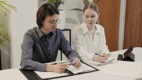 Two colleagues managers sitting at table with documents and tablet in office, discussing work tasks, planning work. teamwork, strategy, collaboration, project, interaction, sharing experience - Powered by Shutterstock - Get 15% off with code: PIKWIZARD15