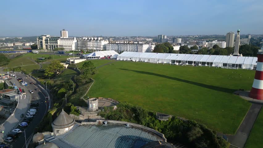 
Plymouth, Devon, England: DRONE VIEW: Track shot across Plymouth Hoe park showing Smeaton's Tower. Plymouth is a port and hosts the largest operational naval base in Western Europe (Clip 2 of 2).