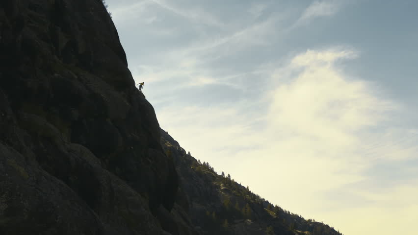Person abseiling on a high rocky mountain wall with rope and helmet in alpine environment, distant view