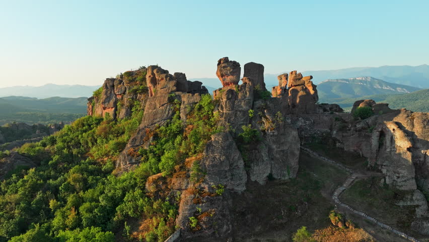 Summer sunrise at Belogradchik Rocks Bulgaria, drone aerial travel view of dramatic cliffs, fortress ruins, green forest landscape, panoramic Balkan mountains, popular nature heritage attraction