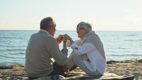 Senior mature couple sitting on beach holding hands enjoying outdoor recreation. Old husband wife touching hands with tenderness love. Grandmother grandfather together. Family moment of love - Powered by Shutterstock - Get 15% off with code: PIKWIZARD15