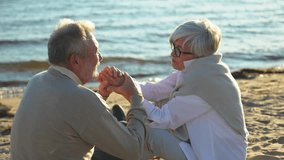 Senior mature couple sitting on beach holding hands enjoying outdoor recreation. Old husband wife touching hands with tenderness love. Grandmother grandfather together. Family moment of love - Powered by Shutterstock - Get 15% off with code: PIKWIZARD15