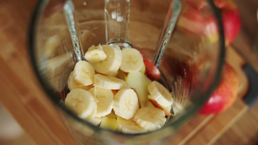 Making healthy detox breakfast smoothie at home. Female hands throws raw broccoli in blender bowl, preparing fresh green vegetarian beverage with banana and apple to cleanse and provide energy body
