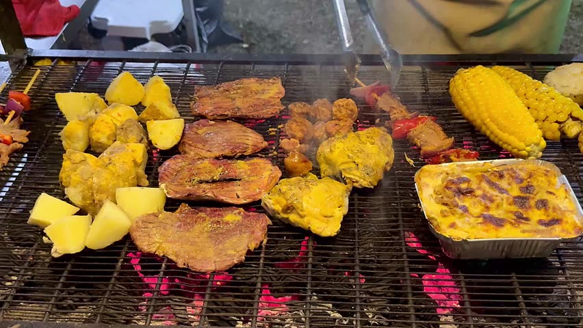 Close-up Colombian barbecue grill with meat, corn, and potatoes cooking over fire