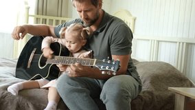 Happy dad teaches his cute daughter to play the guitar while sitting on the sofa in the living room at home. Happy Father's Day. Father teaching his child to play guitar. Kid Learning music skill - Powered by Shutterstock - Get 15% off with code: PIKWIZARD15