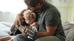 Happy dad teaches his cute daughter to play the guitar while sitting on the sofa in the living room at home. Happy Father's Day. Father teaching his child to play guitar. Kid Learning music skill - Powered by Shutterstock - Get 15% off with code: PIKWIZARD15
