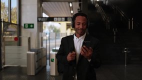 Businessman walking in subway station using smartphone and headphones - Powered by Shutterstock - Get 15% off with code: PIKWIZARD15