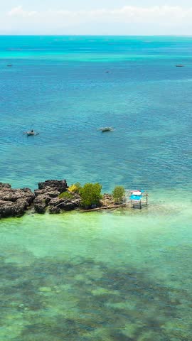 Rocks surrounded by waves and corals. Blue sea with tropical coral reefs. Bantayan Island, Cebu, Philippines. Vertical view.