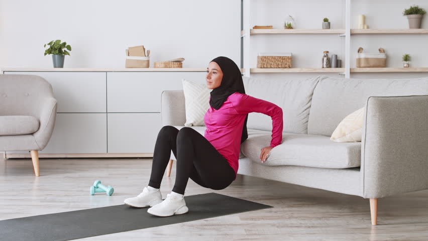 Young Middle Eastern woman exercises at home while wearing a hijab