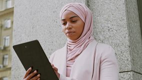 Young Muslim woman in hijab using tablet on urban street in daylight - Powered by Shutterstock - Get 15% off with code: PIKWIZARD15