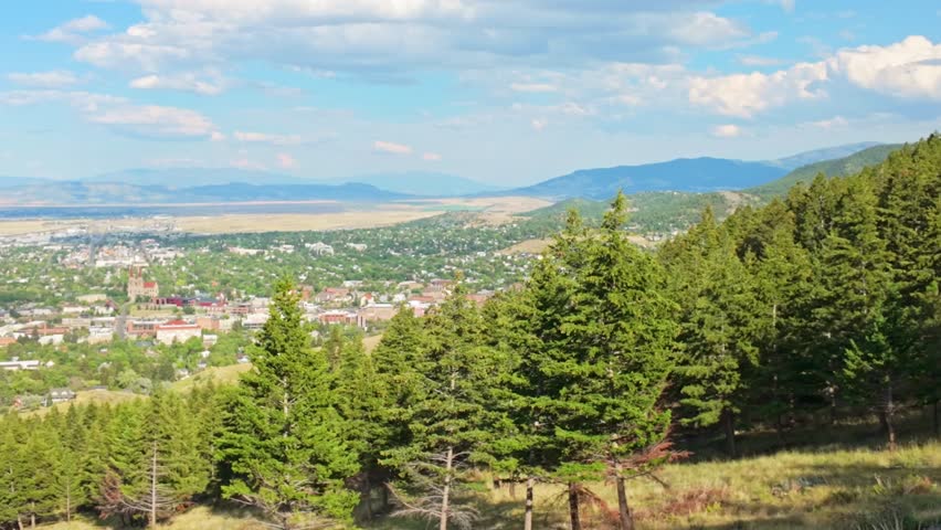 A panoramic aerial view of the city of Helena, Montana is captured at sunset, showcasing the urban landscape