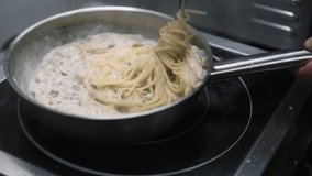 Cooking spaghetti. Noodle meal. Chef hand stirring hot vegetarian dish frying pan by metal tweezers on stove. Tasty pasta in white sauce. - Powered by Shutterstock - Get 15% off with code: PIKWIZARD15