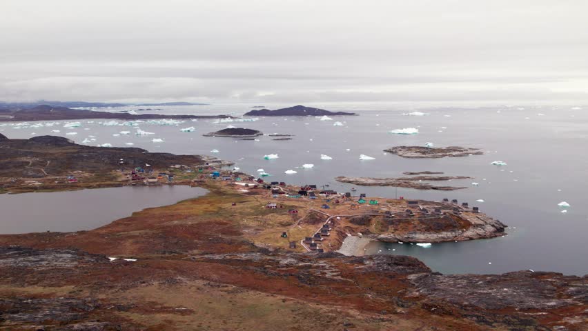 Aerial drone view of the coastal Greenlandic settlement of Ilimanaq, surrounded by Arctic mountains, icy fjords, and the pristine northern seascape.