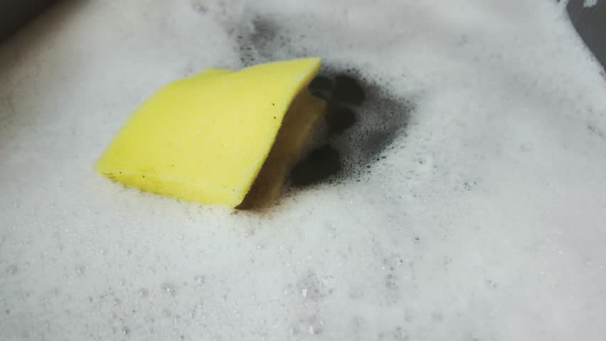 Yellow Dish Washing Sponge floating in foamy soapy water bubbles