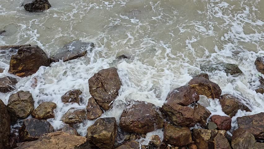 Ocean waves crashing on a rocky shore in a continuous, overhead shot.