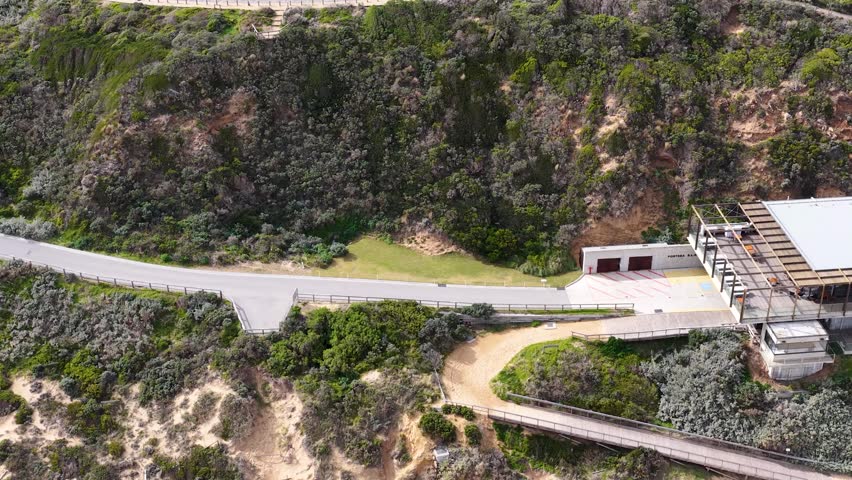 Drone camera glides above cliffside buildings, sandy beach, and approaching ocean waves in daylight - Powered by Shutterstock - Get 15% off with code: PIKWIZARD15