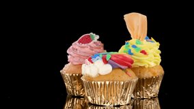 Three colorful gourmet cupcakes rotate on black background under bright studio lighting, close-up view. - Powered by Shutterstock - Get 15% off with code: PIKWIZARD15