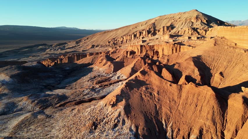 Sweeping 4K drone shot of glowing desert ridges and salt plains surrounding Valle de la Luna at golden hour.