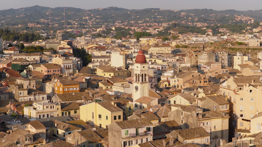 Drone circles around Saint Spyridon Greek Orthodox Church belltower in Old town of Corfu, revealing Corfu old town yacht harbour during sunrise