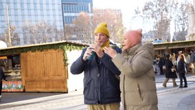 Elderly couple walking arm in arm, drinking hot beverages and enjoying christmas spirit at a winter market - Powered by Shutterstock - Get 15% off with code: PIKWIZARD15