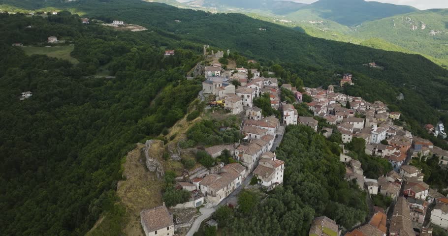 Aerial view of a cluster of houses with red and white roofs clinging to a mountainside, contrasting against the deep green forest, Morcone, Campania, Italy.