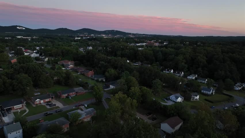Blue hour after Sunset on quaint summer day in American suburb neighborhood. Ascending drone wide shot. Red brick houses and homes in Lynchburg, Virginia. Green trees and yards in well-kept area.