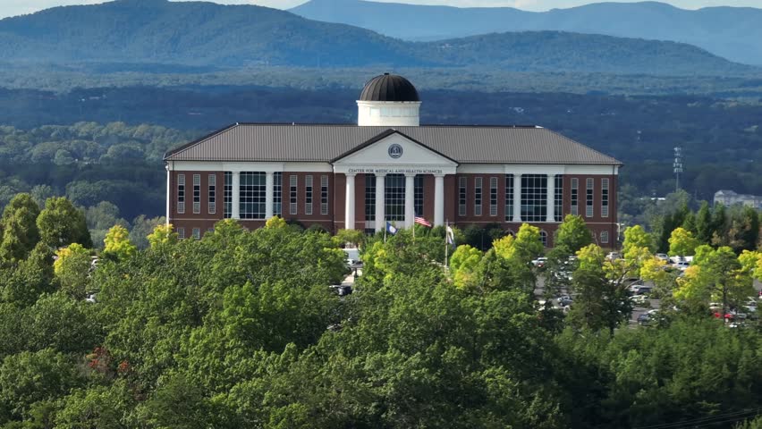 Liberty university college of Lynchburg located on forest hill in summer. Aerial approaching shot. Private campus with parking cars and historic building. Waving American flag on flagpole.