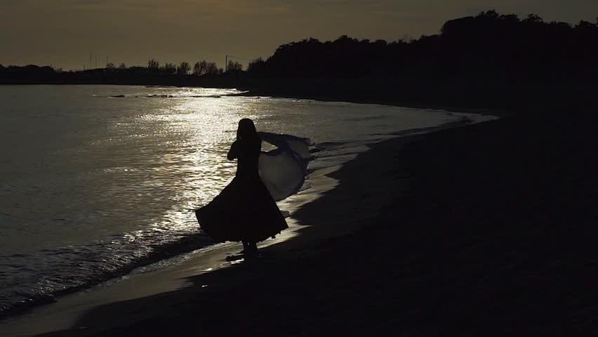 Silhouette of woman dancing on quiet beach at sunset along Adriatic coast with waves gently touching shore