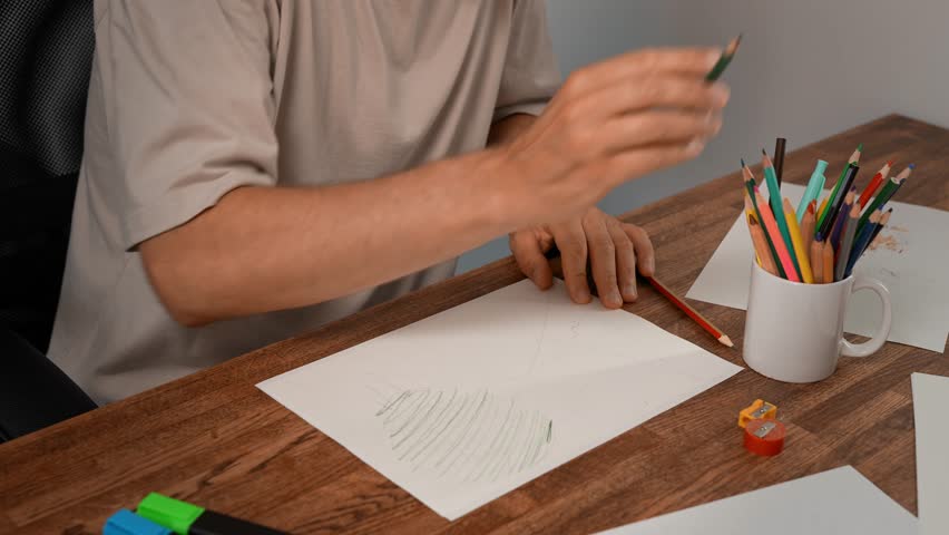 Unrecognizable man drawing with colored pencils. Sharpening pencil with sharpener. Home creativity.