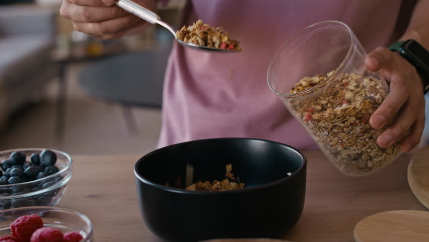 Close up shot of hands of anonymous person preparing healthy breakfast with granola and berries in morning at home
