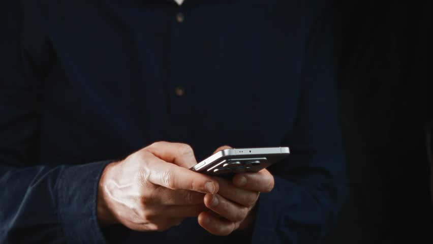 Close-up of smartphone with male hands typing on dark background. Man communicates via social media and work apps, showcasing modern mobile productivity.
