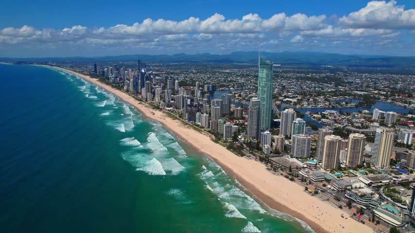 A breathtaking aerial view of Gold Coast, Australia, showcasing the stunning coastline, high-rise skyline, and beautiful sandy beaches. The turquoise ocean waves crash along the shore