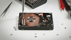 Close-up of disassembled hard drive in repair lab, technician's hands with screwdriver continuing disassembly. Professional data recovery or component-level repair in progress. - Powered by Shutterstock - Get 15% off with code: PIKWIZARD15