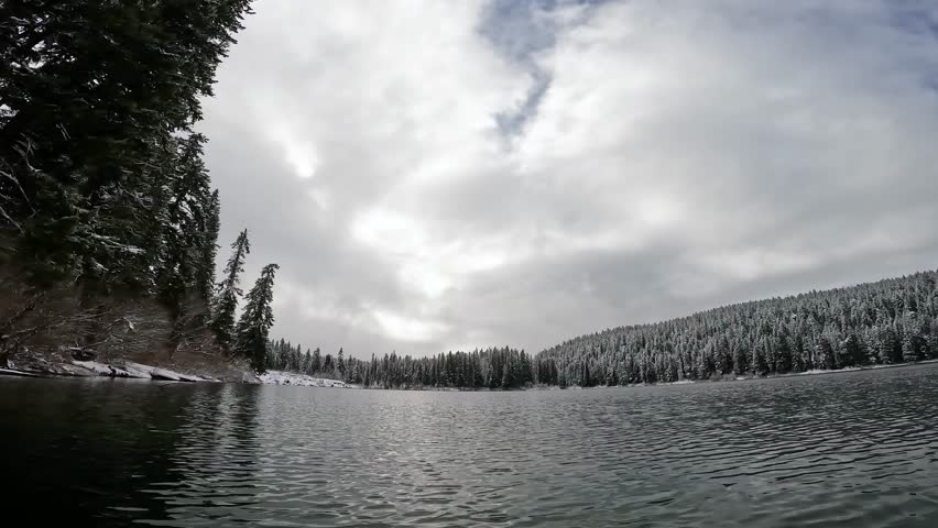 Winter kayaking on Clear Lake along the McKenzie River in Oregon, with snow-covered trees lining the shore under an overcast sky. Peaceful cold weather adventure captured in 4K action camera video