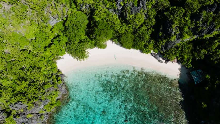 A serene island cove showcasing a beautiful white sandy beach surrounded by green forest. Serenity Beach. El Nido. Palawan, Philippines.