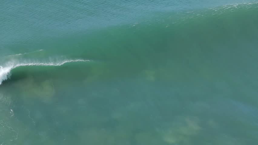 Aerial view of the powerful ocean wave cresting and curling near Nobbys Beach, with turquoise waters contrasting against the white foam, Newcastle, Australia.