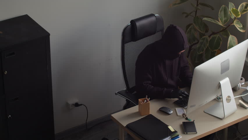 High angle shot of male criminal installing bugging device into desktop telephone spying on confidential corporate data with partner hacking into computer in office room
