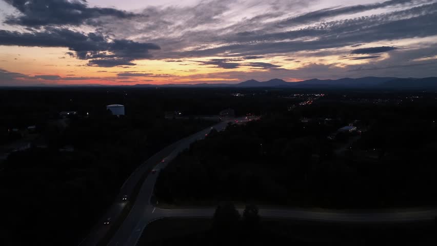Beautiful American sunset over quiet highway, with glowing skies above blue ridge mountains in Virginia. Traffic lights creating peaceful vibes and dynamic evening atmosphere. Aerial wide shot.
