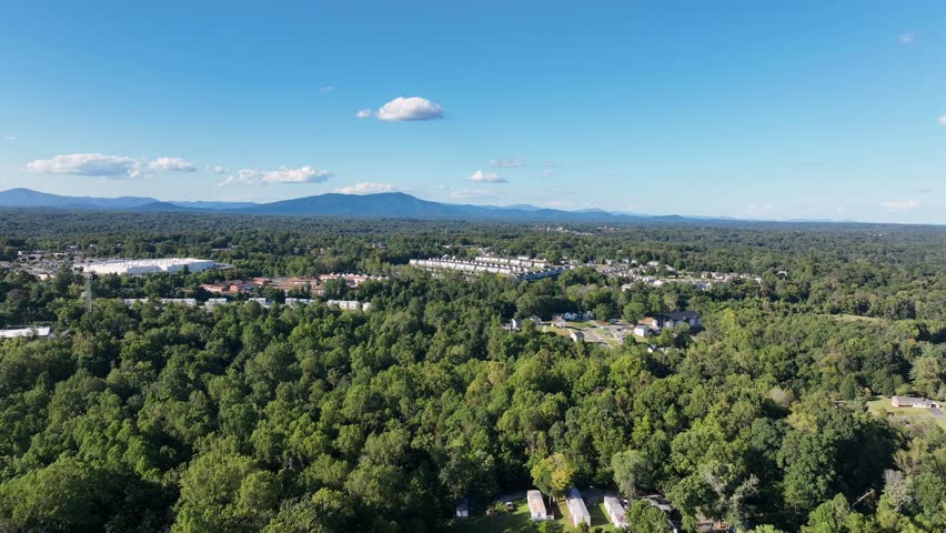 Peaceful suburb neighborhood of forest trailer park with mobile homes during Sunny day in summer. Descend drone wide shot. Blue ridge mountains in background. Blue sky in summer. Lynchburg, Virginia.